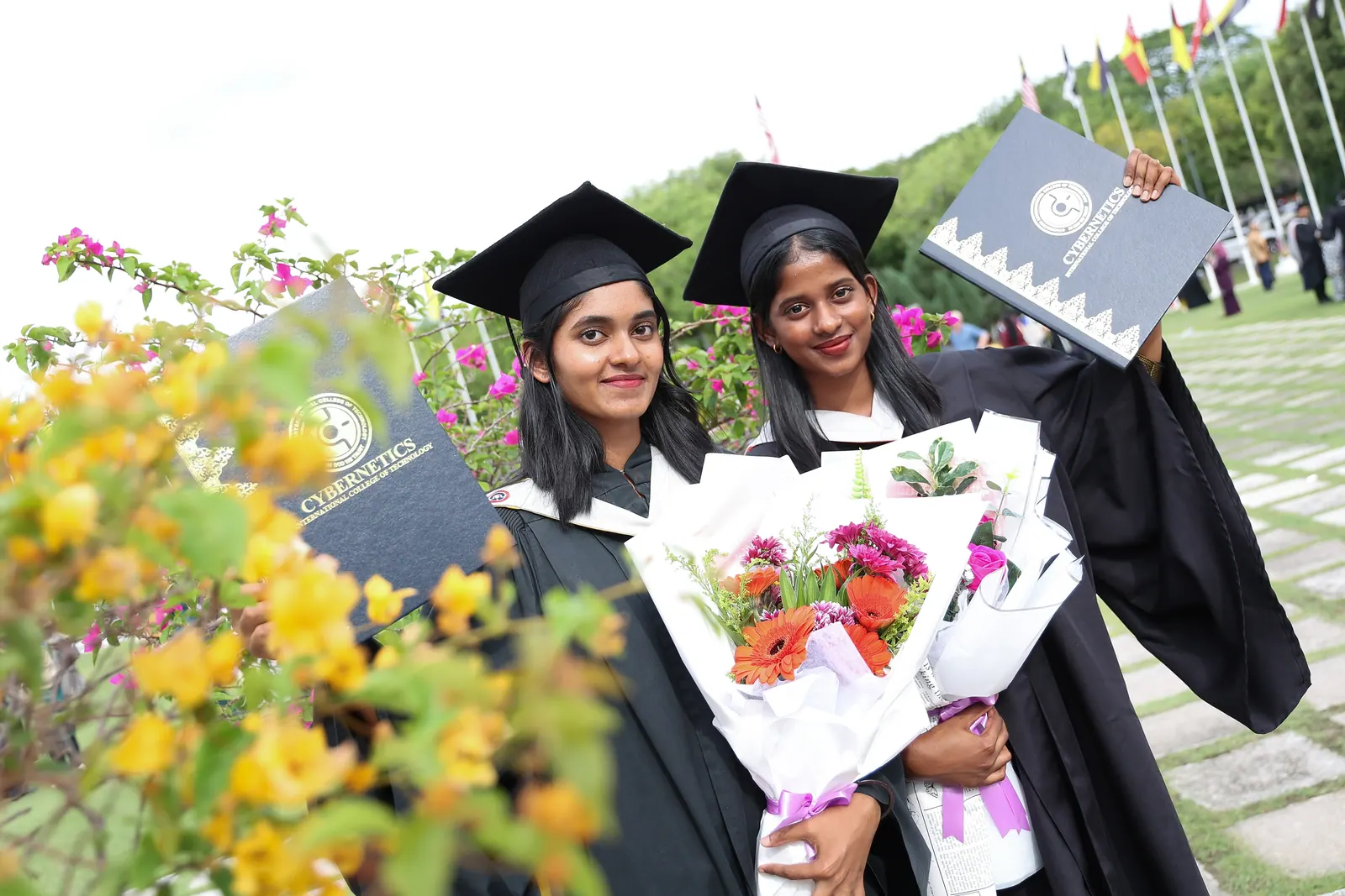 Two KTAC women graduates posing with flowers and certificate folders after convocation